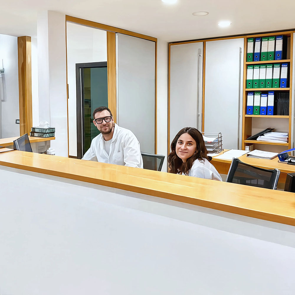 Personale sanitario sorridente alla reception dello studio oculistico, uomo e donna in camice bianco dietro il bancone di accoglienza
