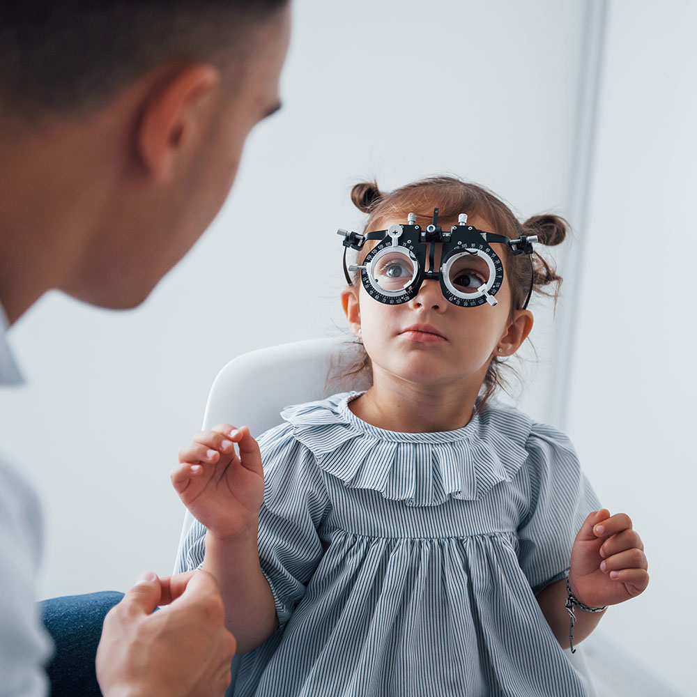 Bambina con occhialino di prova per esame della vista pediatrico, seduta davanti all'oculista durante la visita oftalmologica