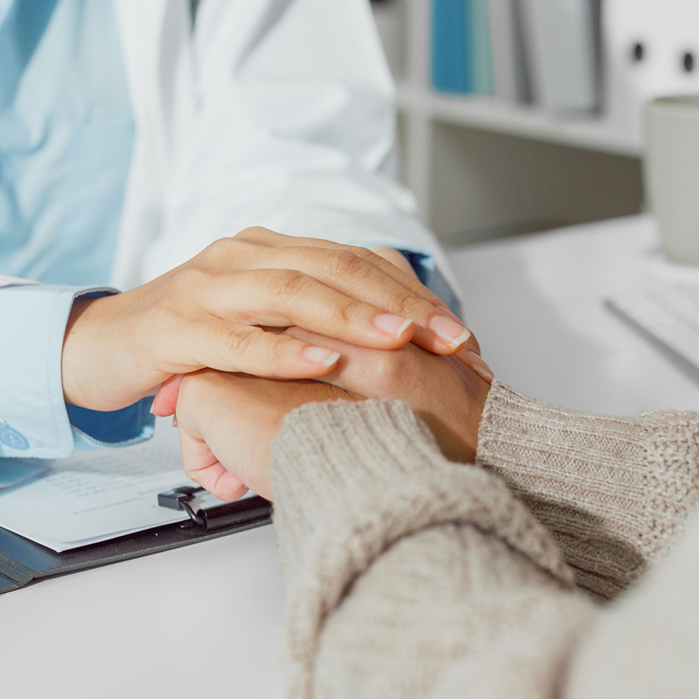 Medico stringe con entrambe le mani la mano di un paziente in segno di conforto, durante una visita in studio